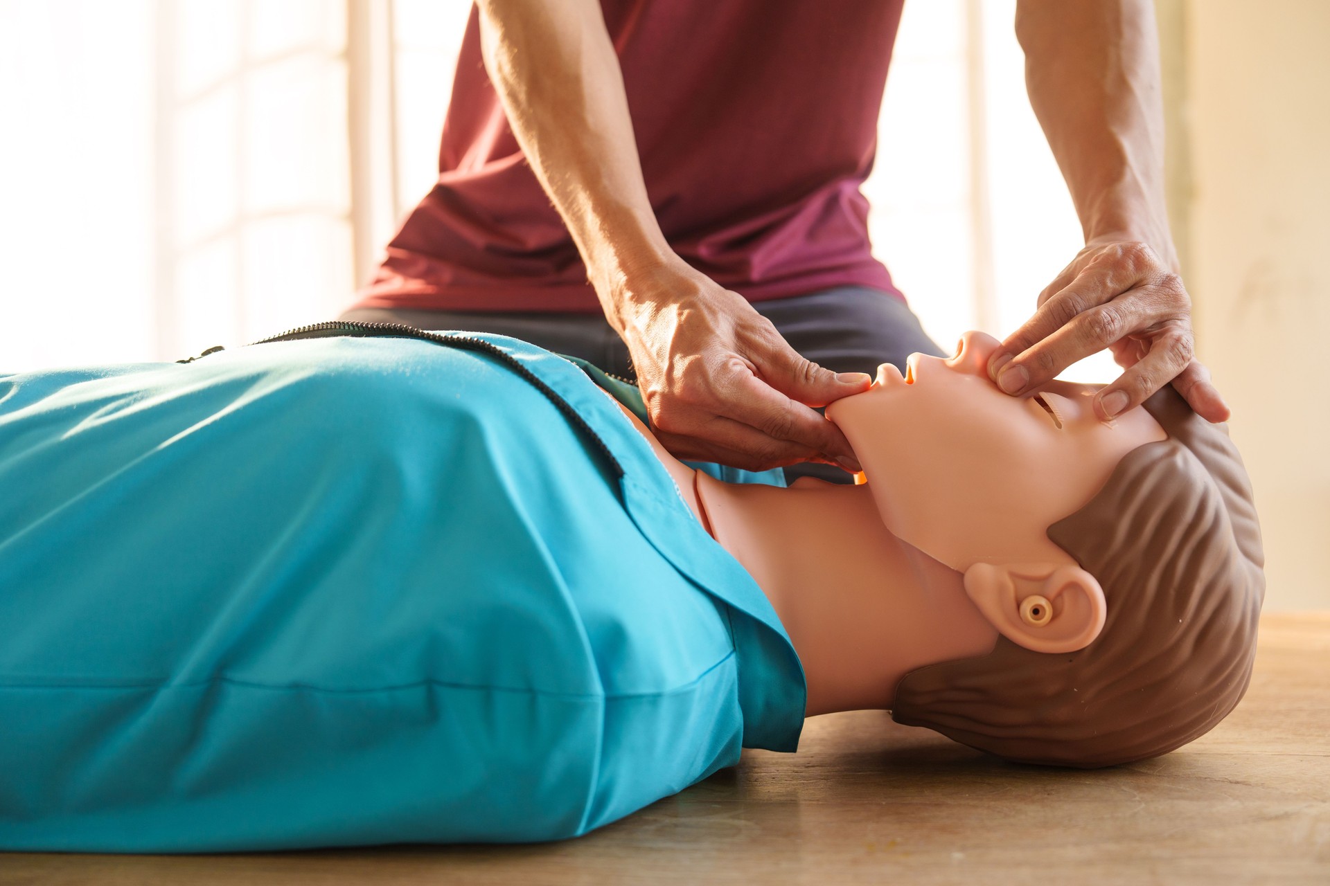 Close-up of middle-aged Asian male hands performing cardiopulmonary resuscitation (CPR) on a training dummy. Vital techniques include defibrillation, chest compressions, and maintaining the airway.